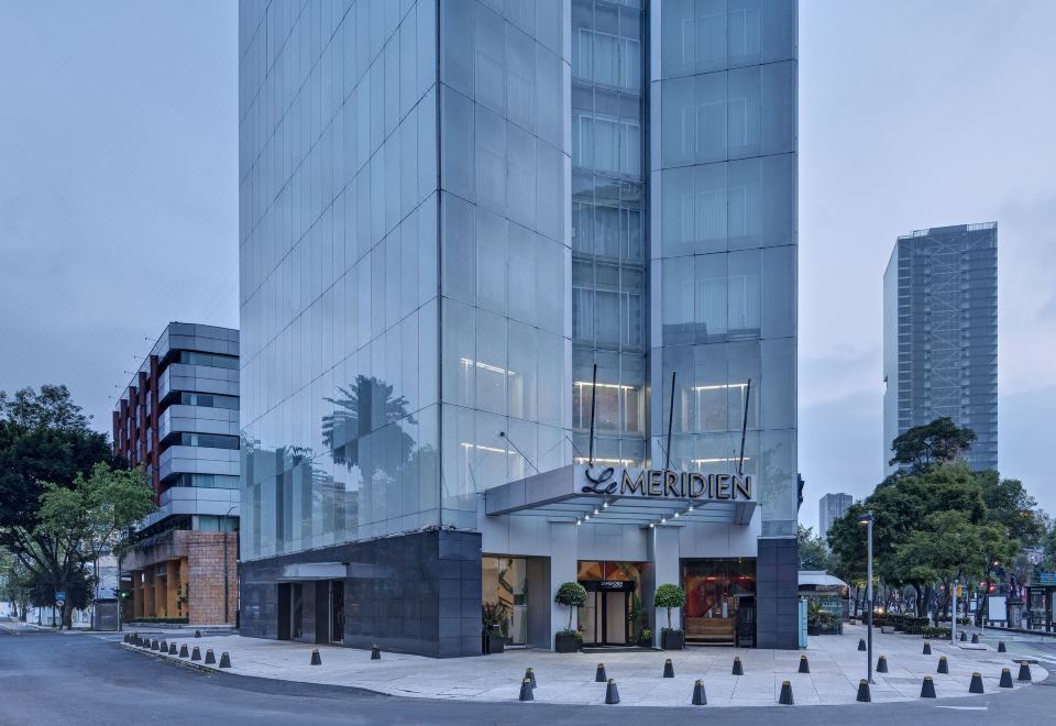 a tall building with a large glass facade is reflected in the window of a store at Le Meridien Mexico City