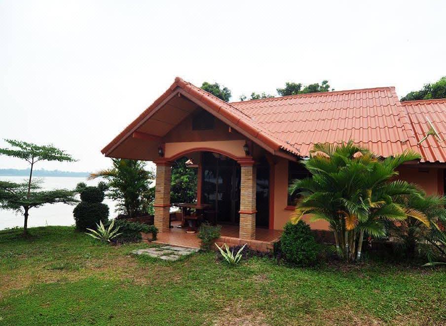 a small wooden house surrounded by a lush green garden , with a lake visible in the background at Baan Rim Khong Resort