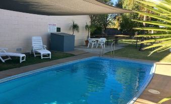 a backyard with a swimming pool surrounded by chairs and a dining table , as well as a patio area with a lounge chair and a dining table at Balonne River Motor Inn