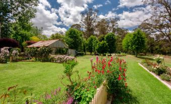 a lush green lawn surrounded by trees , with a small wooden house in the background at Berrima Bakehouse Motel