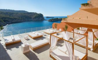 a rooftop terrace with white lounge chairs , umbrellas , and a view of the ocean , set against a clear blue sky at Ole Galeon Ibiza