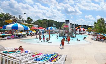 a group of people enjoying a day at an outdoor water park , with various water slides and umbrellas providing shade at Holiday Inn Statesboro-University Area
