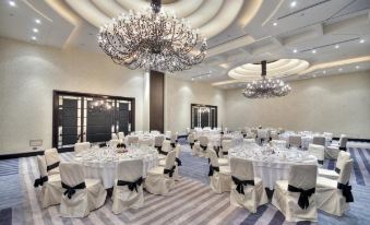 a large , well - lit room with multiple dining tables covered in white tablecloths and chairs arranged for a formal event at AX The Palace
