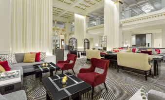 a modern , luxurious lounge area with red chairs and white walls , featuring large windows , black and white striped flooring , and gold details at Hilton Boston Park Plaza