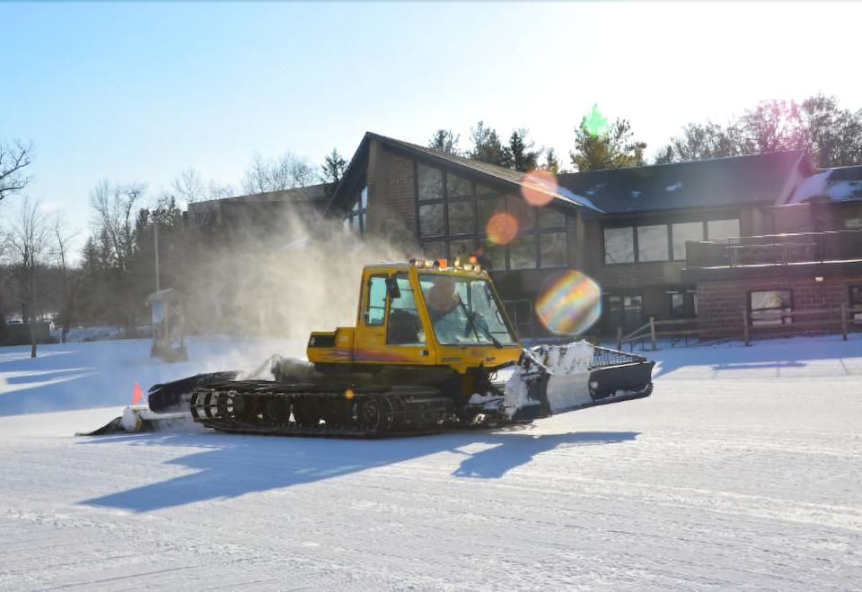 a yellow snowplow is driving through a snow - covered field next to a building , creating a cloud of snow at Devil's Head Resort