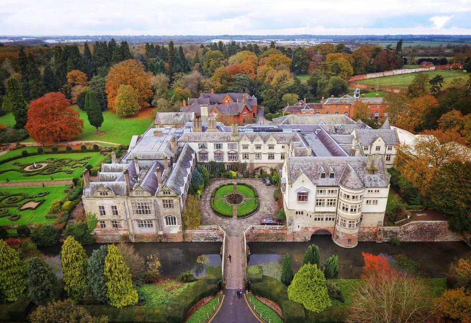 aerial view of a large , ornate building surrounded by trees and grass , with a lake in the background at Coombe Abbey Hotel