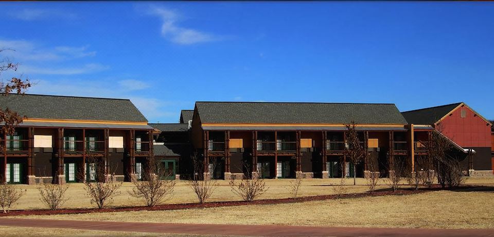a large wooden building with multiple floors and balconies , situated on a dirt road under a clear blue sky at Quartz Mountain Resort