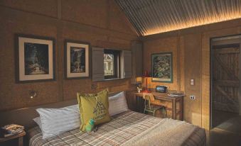 a cozy bedroom with a wooden bed , a desk , and a television mounted on the wall at The Headwaters Eco Lodge