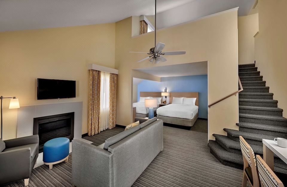 a modern hotel room with a comfortable bed , two beds , and a living area with a couch , fireplace , and stairs leading to the upper at Suites Birmingham
