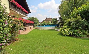 a large , well - maintained green lawn with a swimming pool in the background , surrounded by trees and flowers at Anita