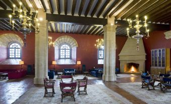 a spacious , well - lit living room with wooden beams and red walls , featuring multiple chairs , couches , and a fireplace at Parador de Siguenza