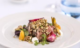 a white plate with a delicious meal consisting of meat , vegetables , and nuts , placed on a dining table at Hotel Grand Chancellor Brisbane
