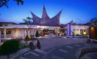 a hotel entrance with a large thatched roof , surrounded by trees and lit up at night at Aston Sunset Beach Resort - Gili Trawangan