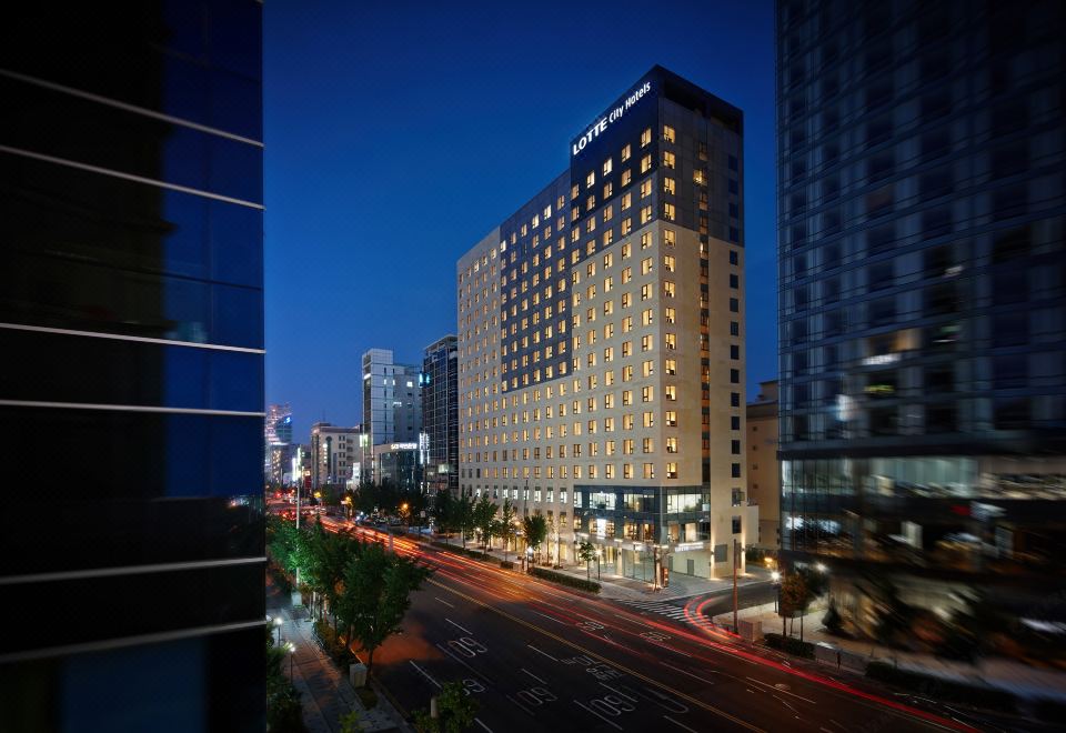 a tall building with a distinctive design is lit up at night , with a busy city street below at Lotte City Hotel Ulsan