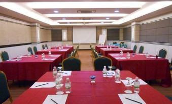 a large conference room with multiple tables and chairs , each table set with red tablecloths and water bottles at HIG Hotel