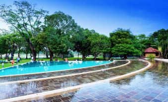 a large outdoor swimming pool surrounded by trees , with people enjoying their time in the water at Habarana Village by Cinnamon