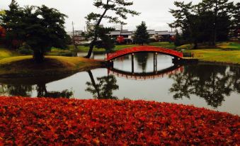 a red bridge with a reflection of the bridge in a body of water , surrounded by trees and flowers at Nara Hotel