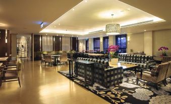 a well - lit hotel lobby with a large dining table , chairs , and couches arranged in a lounge - like setting at Sol Hotel