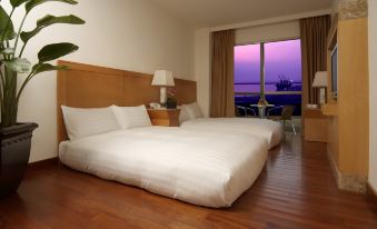a large bed with white sheets and pillows is in a room with wooden floors and a window overlooking the ocean at Ocean Hotel