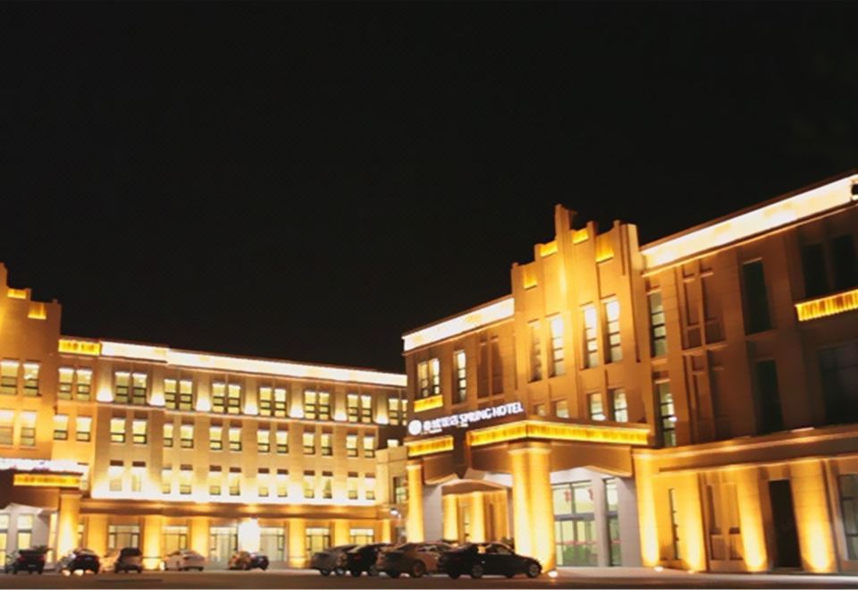 a large , modern building with multiple floors and balconies , lit up at night , surrounded by trees at Spring Hotel