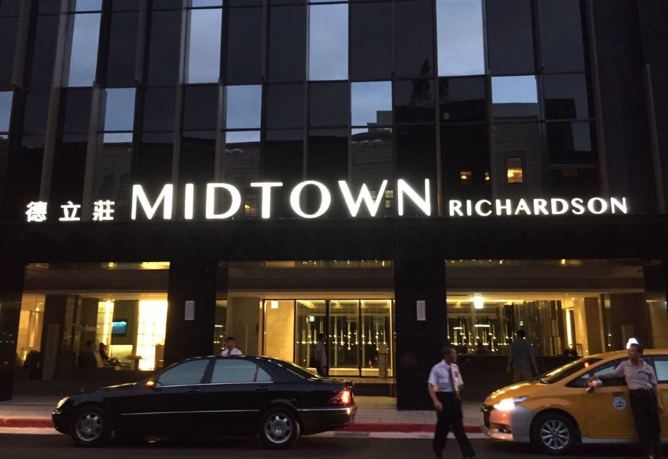 At night, there is a building with the entrance to an upscale hotel and cars parked in front at Hotel Midtown Richardson