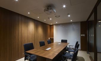 A conference room is illuminated by recessed lighting, featuring wooden walls and black chairs arranged around a long table at Hotel Venue-G Seoul
