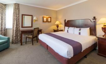 a large bed with a purple and white comforter is in the middle of a room with a desk , chair , and lamps at Holiday Inn Glasgow - East Kilbride