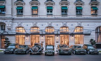 a row of vintage cars parked in front of a building with large windows and green awnings at Hotel the Peninsula Paris