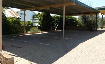 a large , empty parking lot with a metal roof and a carport in the background at Adelong Motel
