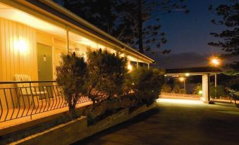 a well - lit building with trees and a staircase leading up to it , bathed in the warm glow of lights at night at Waterview Gosford Motor Inn