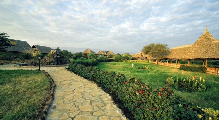 a stone pathway leads through a lush green landscape with trees and houses in the background at AA Lodge Amboseli