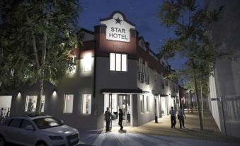 a nighttime scene of a hotel entrance with people walking in front of it , surrounded by trees at The Star Apartments