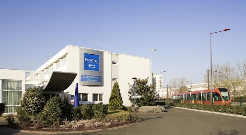 a large white building with a blue sign on the front , located in a residential area at Novotel le Mans