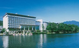 a large white hotel building situated on the edge of a lake , with a beautiful view of the lake and surrounding trees at New Akan Hotel