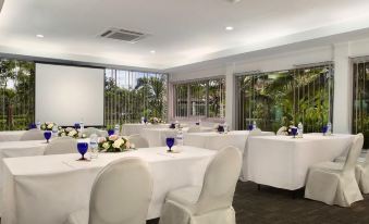 a well - organized conference room with white tables and chairs , along with a projector screen and windows at Delonix Hotel Karawang