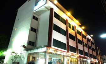 a modern building with multiple floors , lit up at night , and a person standing in front of the entrance at White Inn Nongkhai Hotel