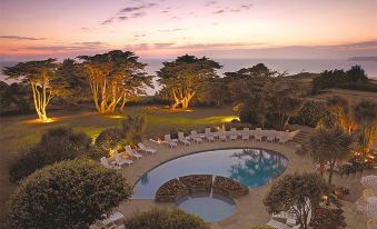 an aerial view of a resort with a pool surrounded by trees and a sunset at The Atlantic Hotel