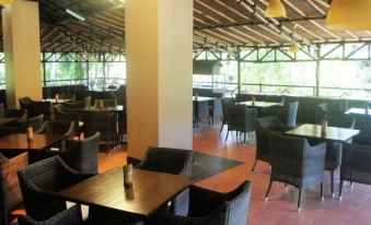 a modern restaurant with wooden tables and chairs , black cushions , and large windows , under a wooden roof at Tasik Ria Resort