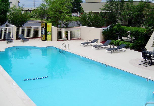 a large swimming pool with lounge chairs and a white wall , surrounded by trees and buildings at Mobile Marriott