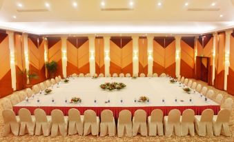 a large banquet hall with a long table surrounded by white chairs and orange walls at Emeralda Resort Ninh Binh