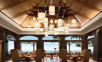 a large dining room with wooden tables and chairs , a chandelier , and a view of the ocean at Four Seasons Resort Lana'i