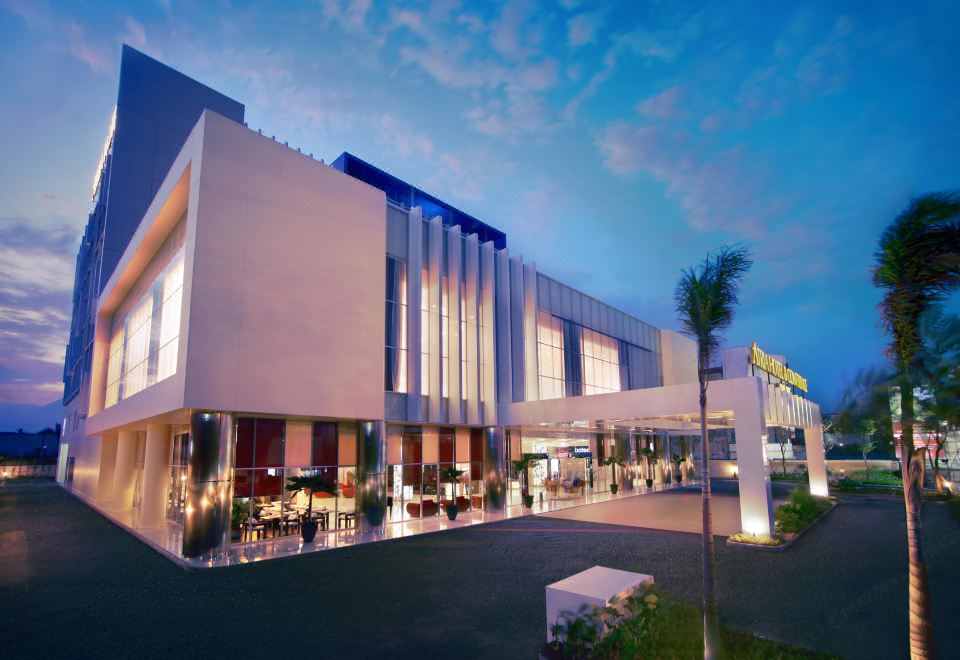 a large building with a modern design , possibly a hotel or an office building , surrounded by palm trees and lit up at night at Atria Hotel Malang