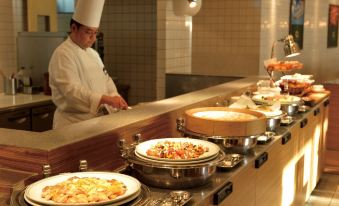 a chef in a white hat is standing behind a counter with several plates of food at Loisir Hotel Naha